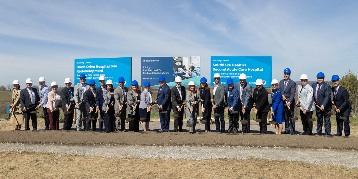 A large group of people wearing hardhats, holding shovels at a sod turning event 