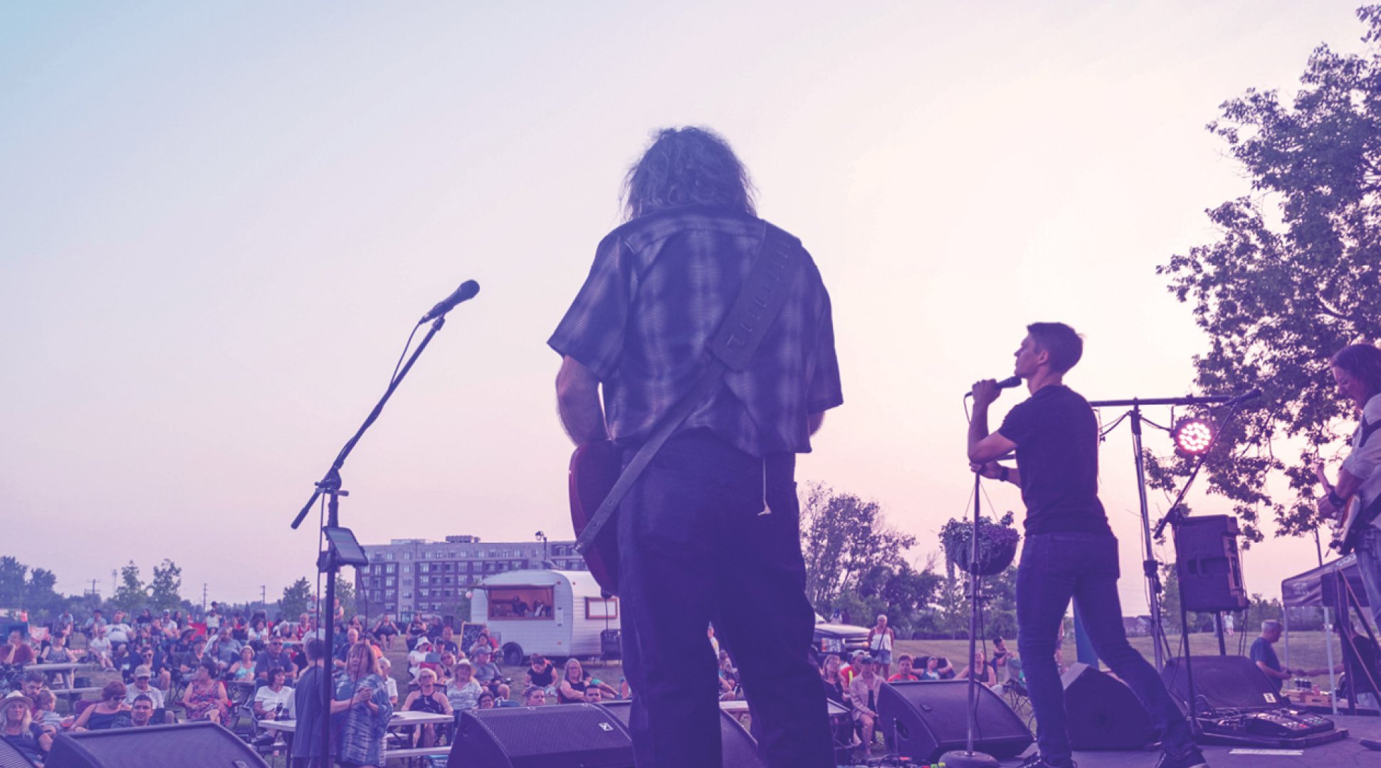A band on stage looking out at the crowd on a summer day