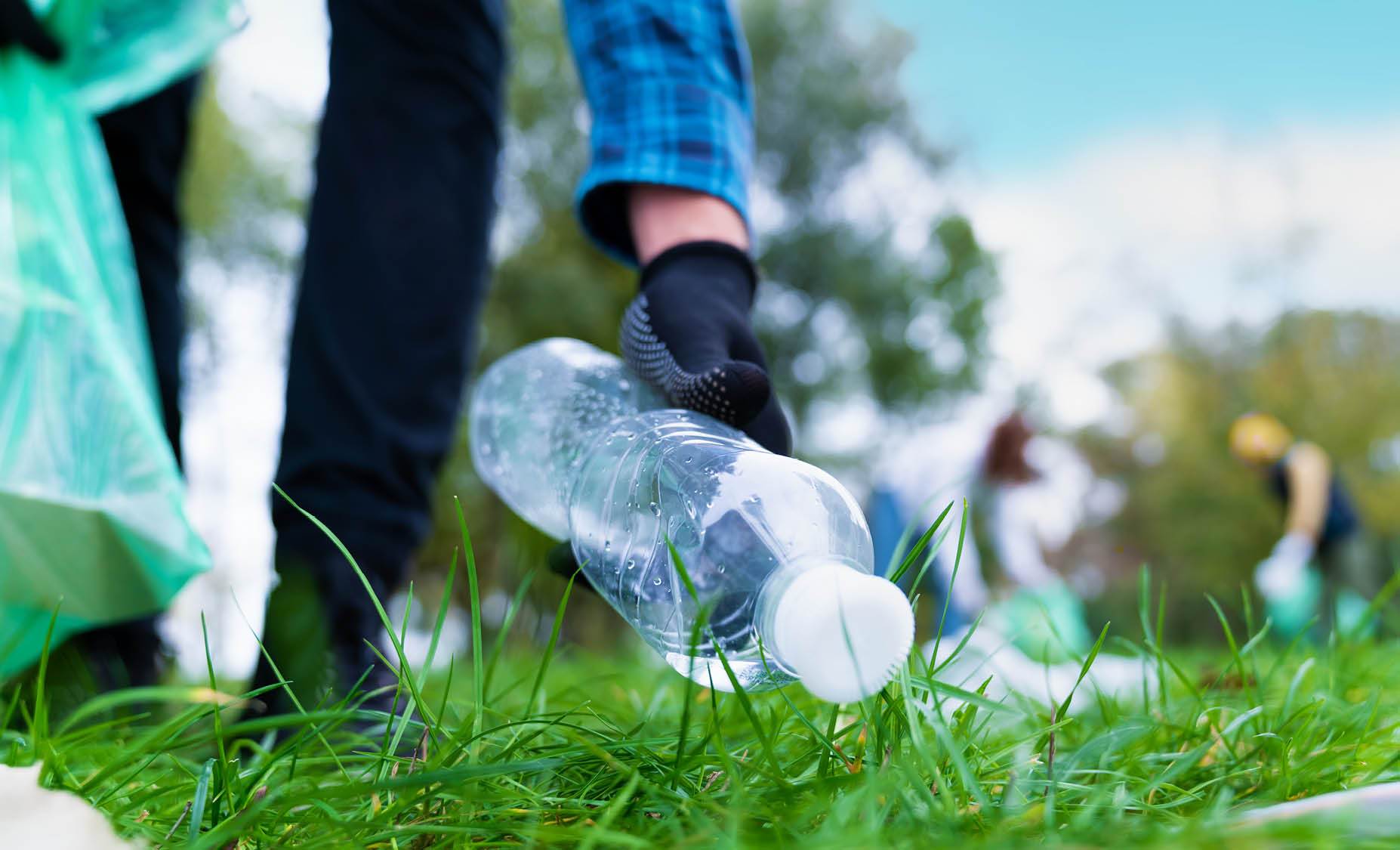 Person picking up used water bottle in park 