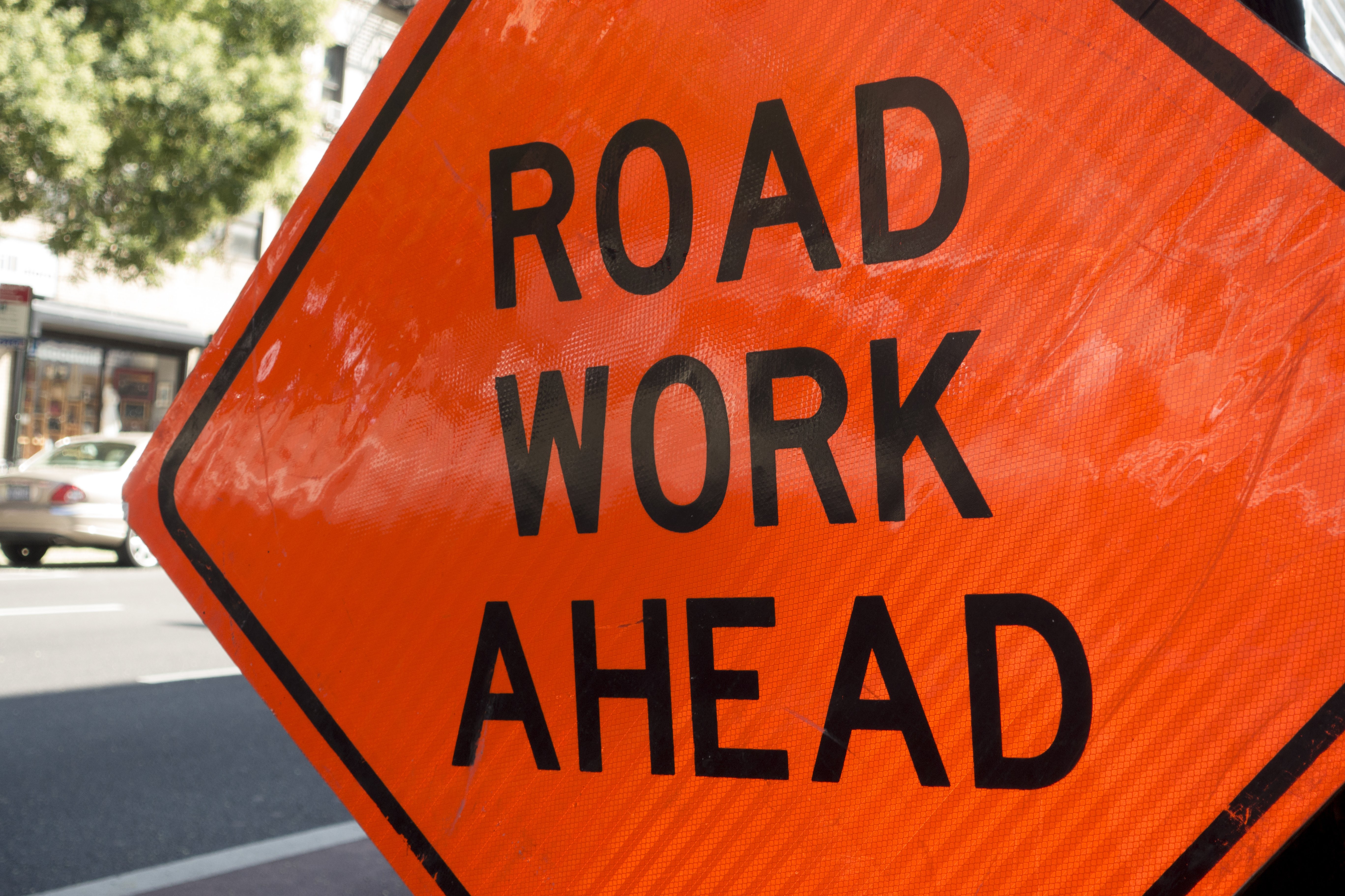 photo of an orange construction sign that reads: Road Work Ahead