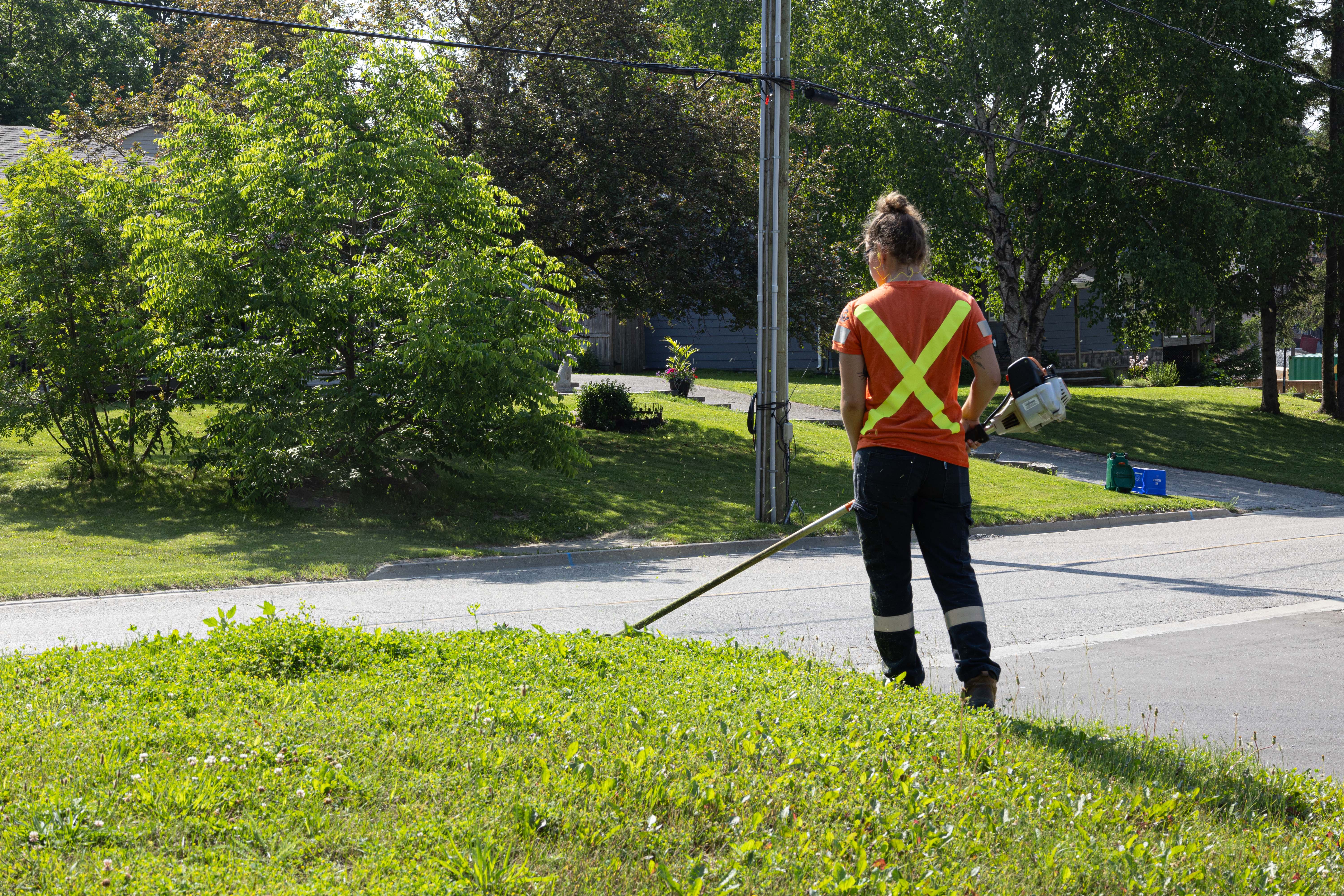 Person cutting grass with a trimmer in an orange tshirt