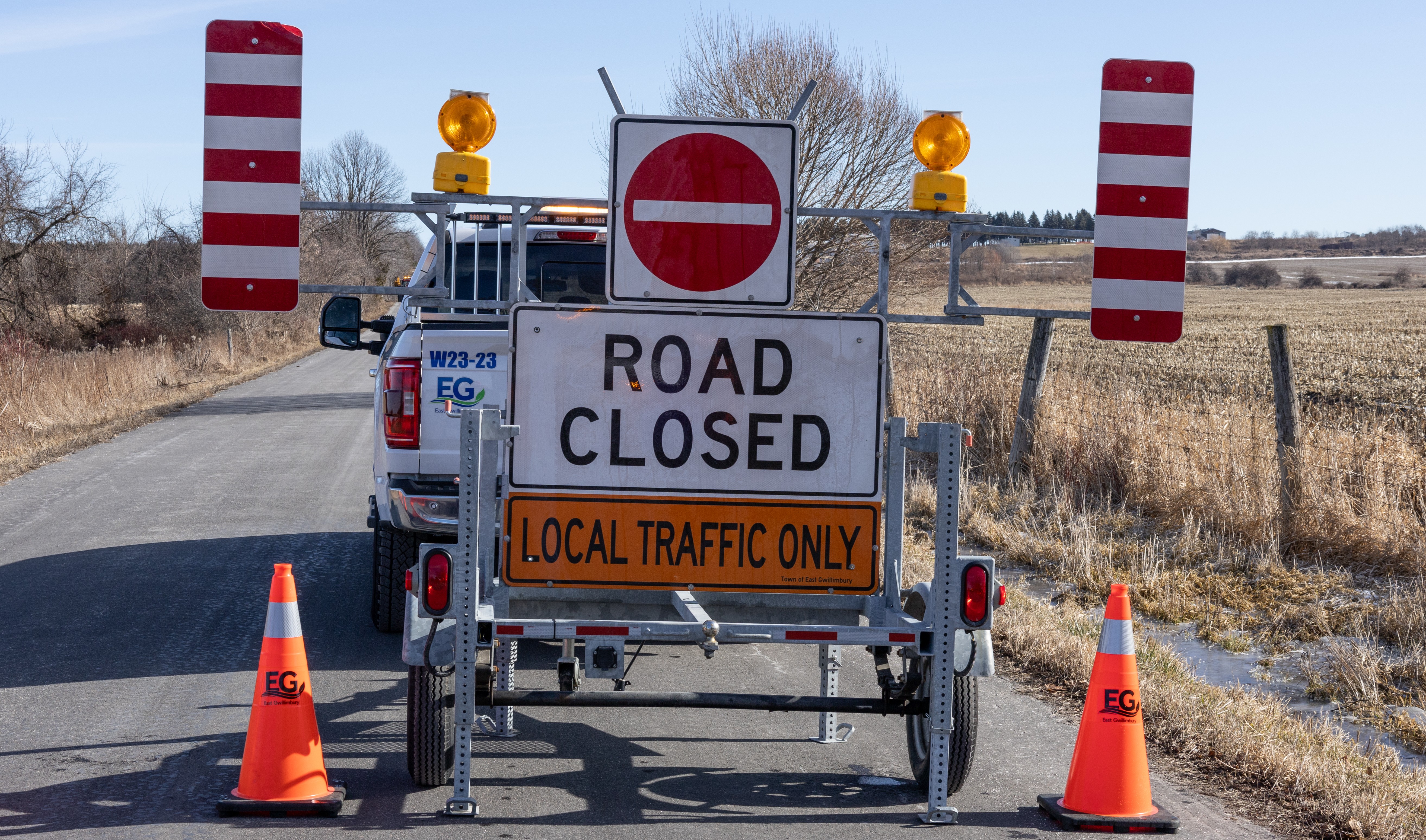 road closure signs blocking a road next to a field