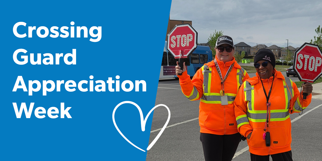 Crossing guards wearing safety vests and holding a stop signs standing next to each other near a crosswalk. 